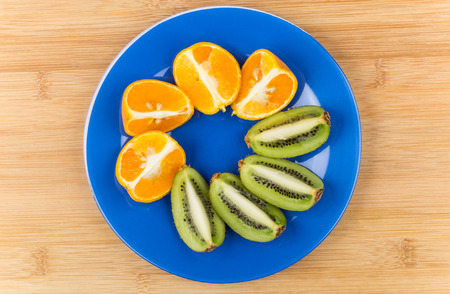 Blue glass plate with slices of tangerines and kiwi on wooden tableの写真素材