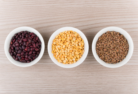 Row of bowls with red beans, dry peas and lentils on wooden table, top viewの写真素材
