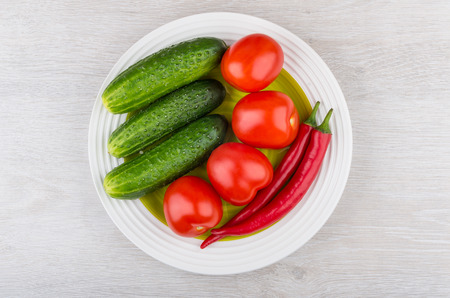 Tomatoes, cucumbers and red hot chili peppers in green glass plate on wooden table. Top viewの写真素材