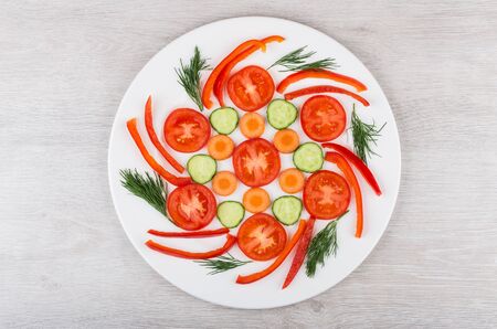 Slices of miscellaneous vegetables and dill in white glass plate on wooden table. Top viewの写真素材