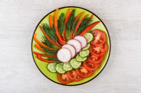 Slices of miscellaneous vegetables and dill in green glass plate on wooden table. Top viewの写真素材