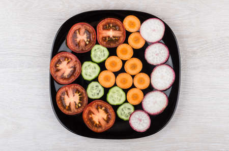 Slices of tomatoes, radishes, cucumbers and carrots in black glass plate. Top viewの写真素材