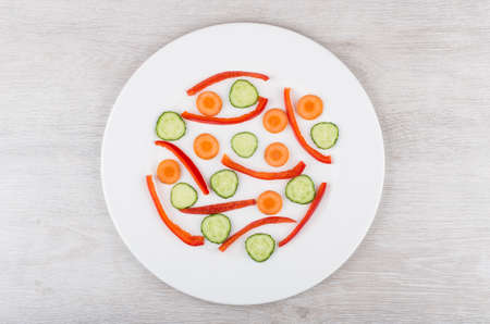 Slices of peppers, carrots and cucumbers in white glass plate on wooden table. Top viewの写真素材