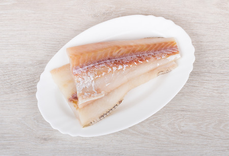Raw fillets of pollock in plate on wooden table. Top view