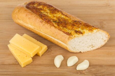 Baguette, garlic and pieces of cheese on wooden tableの写真素材