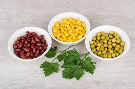 Three bowls with green peas, beans, sweet corn and parsley on wooden tableの写真素材