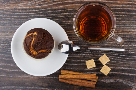 Cupcake in saucer, cinnamon sticks, sugar and tea on wooden table. Top viewの写真素材