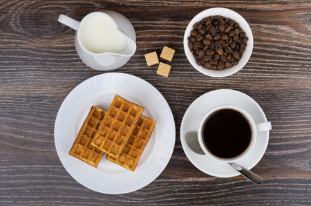 Cup, jug milk, bowl with coffee beans and viennese waffles on wooden table. Top viewの写真素材