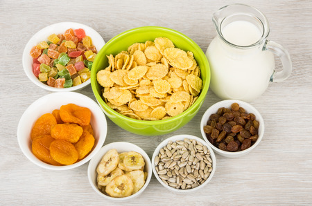 Ingredients for muesli in bowls and jug milk on table