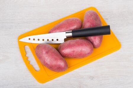 Tubers raw red potato on orange  cutting board and kitchen knife isolated on wooden tableの写真素材