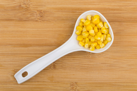 White plastic spoon with sweet corn on wooden table. Top viewの写真素材