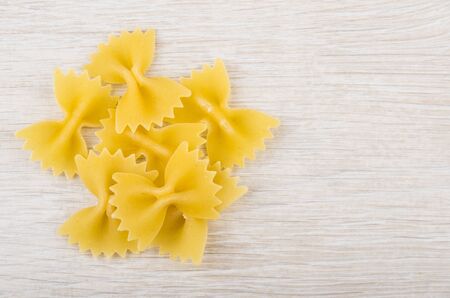 Heap of macaroni farfalle left on wooden table. Top view
