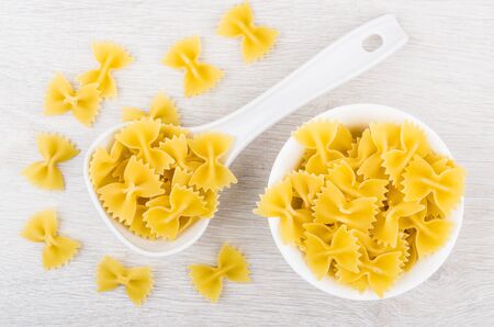 Glass bowl and plastic spoon with macaroni farfalle on wooden table. Top viewの写真素材