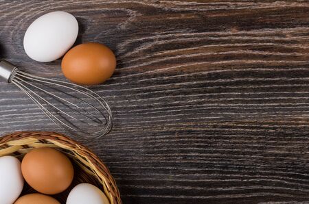 Wicker basket with eggs and whisk from left side on dark table