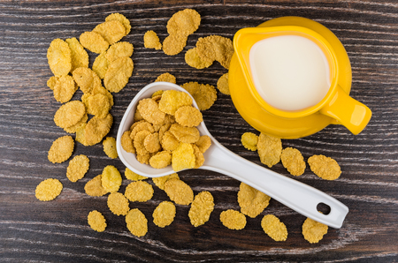 Jug of milk, plastic spoon and scattered flakes on wooden table. Top view