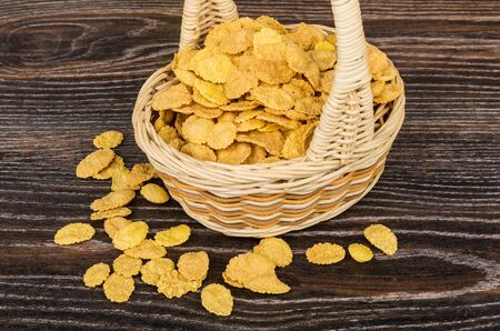 Corn flakes in wicker basket and scattered flakes on wooden table