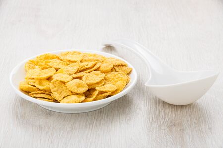 Saucer with corn flakes and white plastic spoon on wooden table