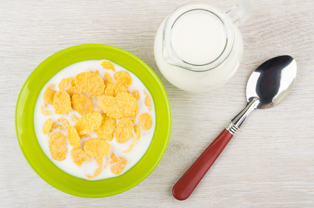 Corn flakes with milk in green bowl, jug and spoon on wooden table. Top viewの写真素材