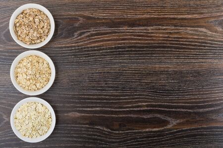 Row glass bowls with oat, rye, barley flakes from left side wooden table. Top view