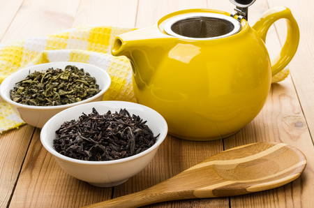 Bowls with dry green and black tea, teapot, spoon on wooden tableの写真素材
