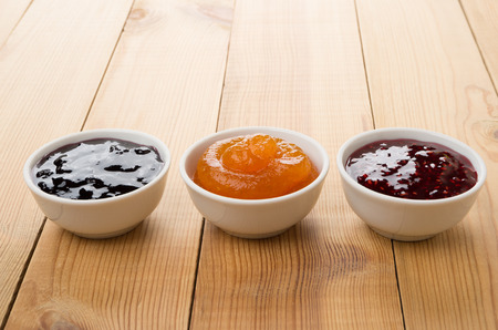 Row of bowls with raspberry, peach, blueberry jam on wooden tableの写真素材