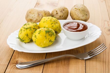 Baked potatoes with dill, ketchup on dish and fork on wooden tableの写真素材