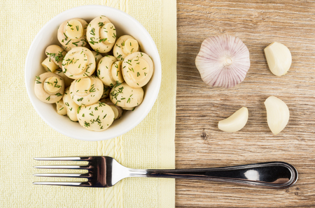 Marinated champignons with dill in bowl, slices of garlic and fork on wooden table. Top viewの写真素材