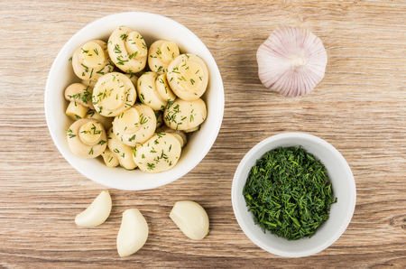Glass bowl with marinated champignons, bowl with dill and slices of garlic on wooden table. Top viewの写真素材