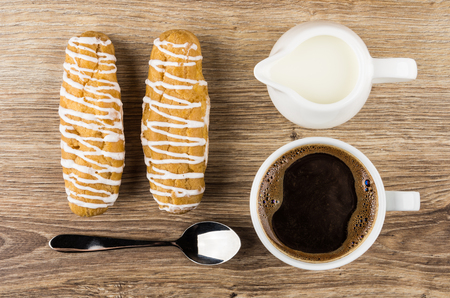 Cup of coffee, jug milk, eclairs and spoon on wooden table. Top view