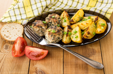 Dish with fried meatballs, baked potatoes, pieces of tomatoes and bread on wooden tableの写真素材