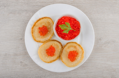 Glass bowl and pancakes with imitation red caviar in plate on wooden table. Top viewの写真素材