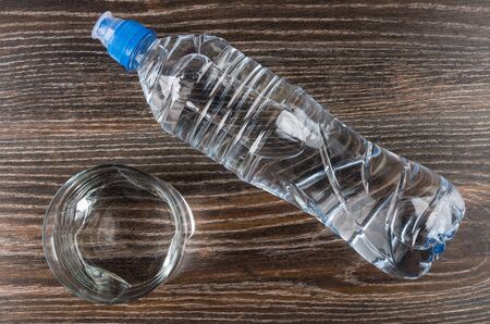Glass water and lying plastic bottle on dark wooden table. Top viewの写真素材