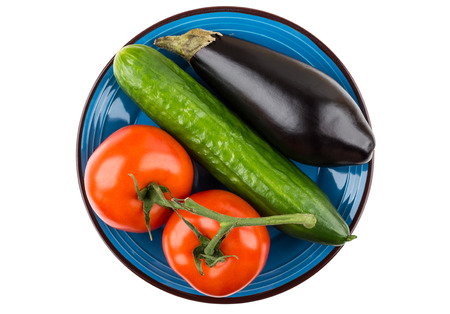 Tomatoes, cucumber and eggplant in blue plate isolated on white background. Top viewの写真素材