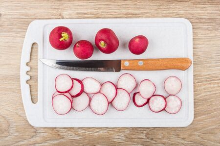 Chopped radishes and kitchen knife on plastic cutting board on wooden table. Top viewの写真素材