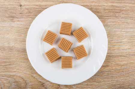 Pieces of creamy toffee in white plate on wooden table. Top viewの写真素材