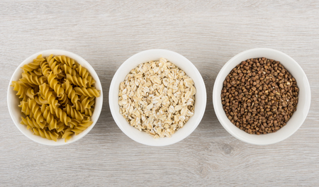 Bowls with pasta, oatmeal and buckwheat - source slow carbs on wooden table. Top viewの写真素材