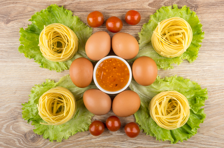 Pasta tagliatelle, lettuce, eggs, tomato cherry and bowl of sauce on wooden table. Top viewの写真素材