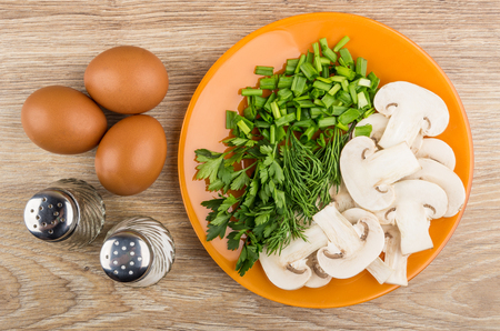 Slices of mushrooms, greens in plate, eggs, salt and pepper on wooden table. Top viewの写真素材