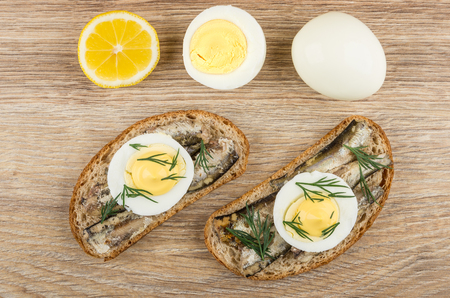 Sandwiches with sparts in oil, eggs, lemon and boiled egg on wooden table. Top viewの写真素材