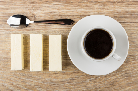 Spoon, row of marshmallow sticks and cup of black coffee on wooden table. Top viewの写真素材