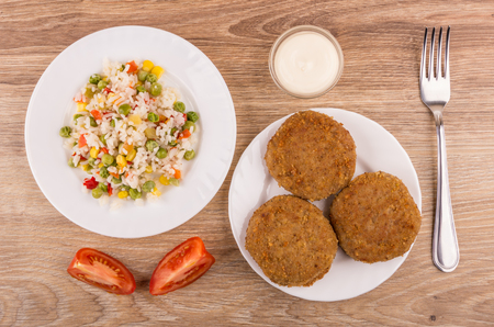 Plates with vegetable mix, fried cutlets, bowl with mayonnaise, tomatoes and fork on wooden table. Top viewの写真素材