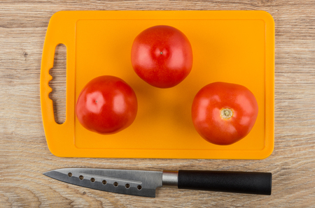 Tomatoes on cutting board and kitchen knife on wooden table. Top viewの写真素材