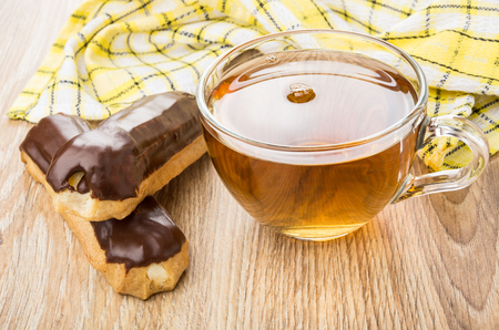 Eclairs, tea in transparent cup and yellow napkin on wooden table