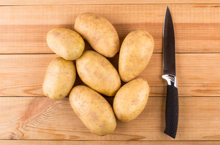 Heap of raw washed potatoes and kitchen knife on wooden table. Top viewの写真素材