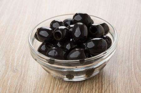Black olives in transparent bowl on wooden tableの写真素材
