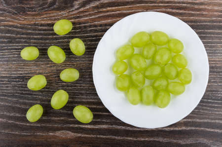 Berries of ripe grape in white plate and on dark wooden table. Top viewの写真素材