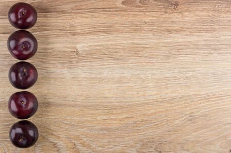 Row of ripe plums from left side wooden table. Top viewの写真素材