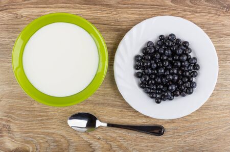 Bowl with yogurt, plate with blueberries and spoon on wooden table. Top viewの写真素材