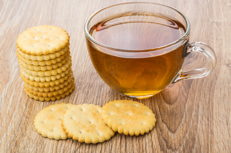 Stack of crackers and transparent cup with tea on wooden tableの写真素材