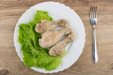 Fried chicken legs, leaves of lettuce in plate and fork on wooden table. Top viewの写真素材
